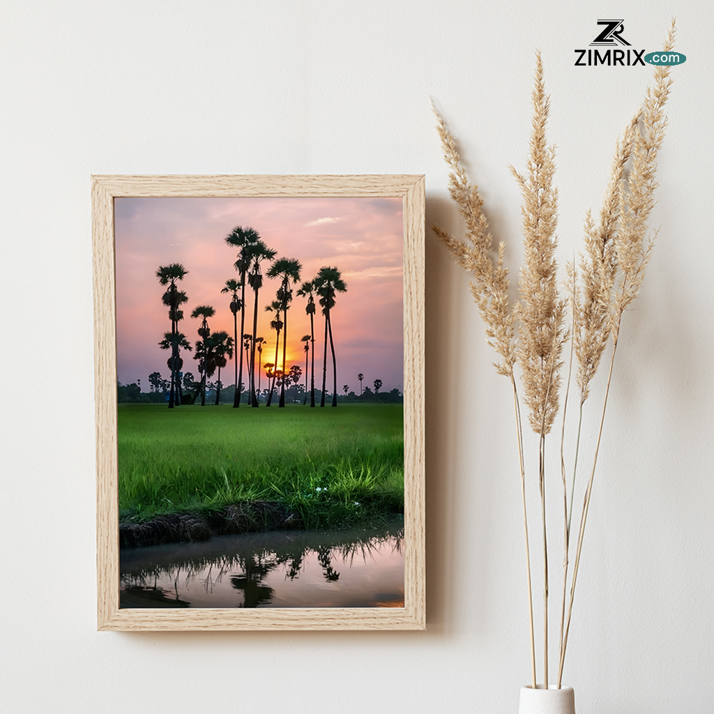 Sunset behind palm trees with reflection on water amidst green fields.