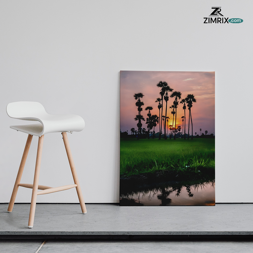 Sunset behind palm trees with reflection on water amidst green fields.